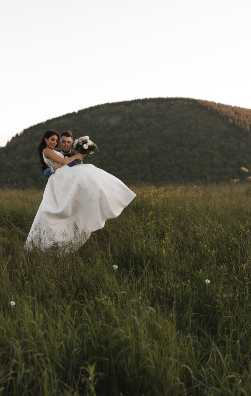 groom carrying bride through green field